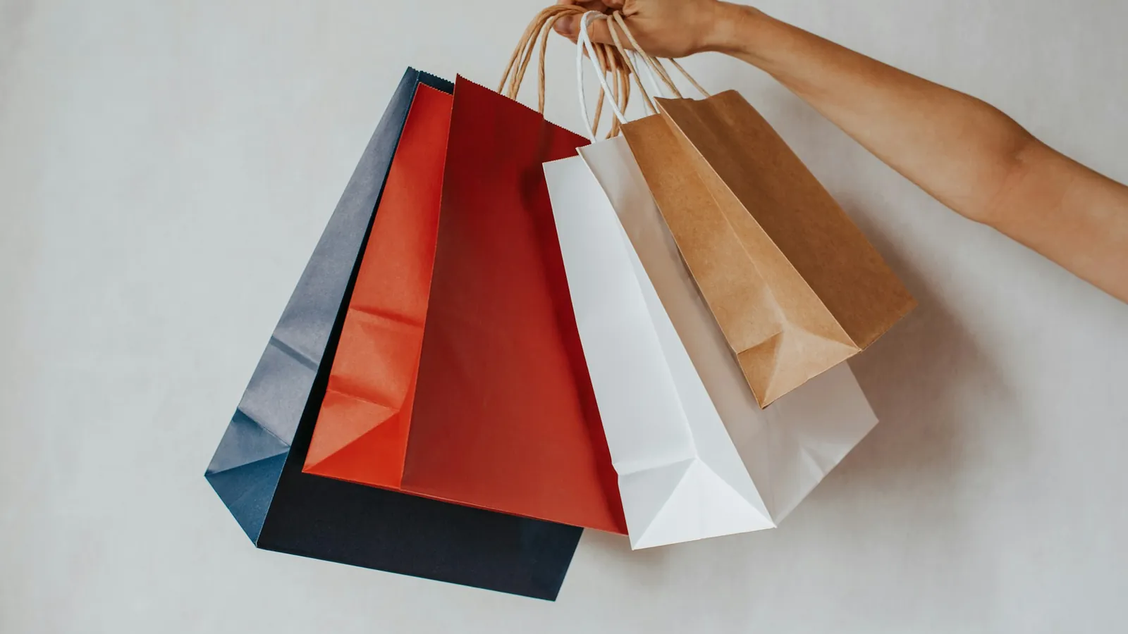 A hand holding a bunch of colourful paper shopping bags