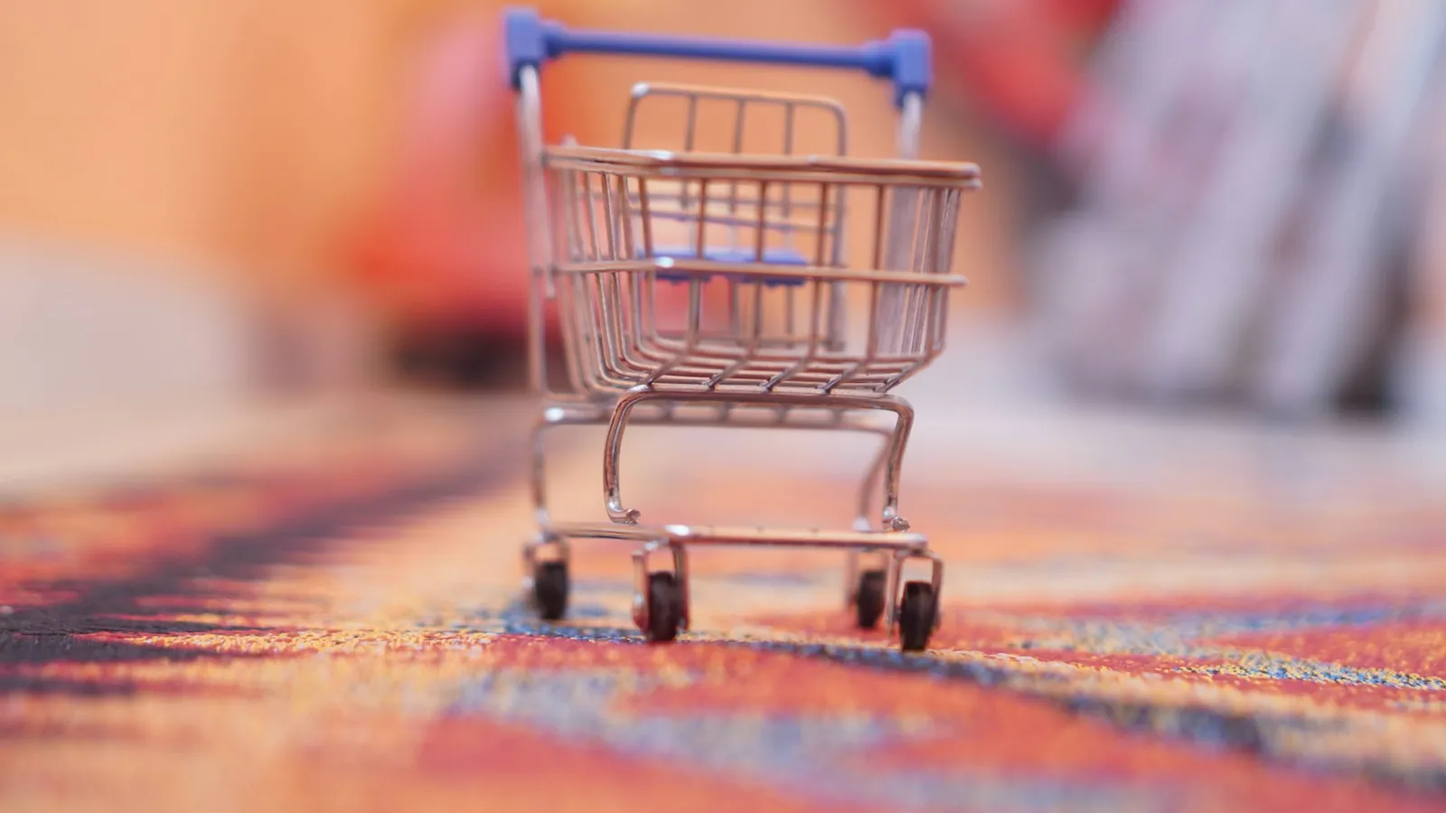 A miniature shopping trolley on a soft, colourful blurred background