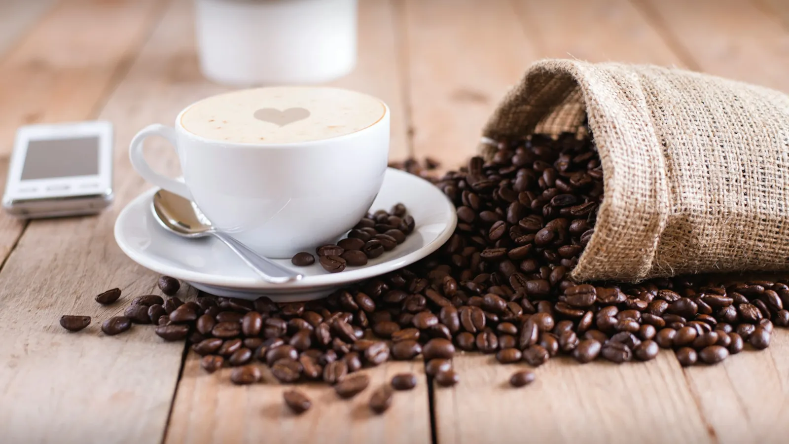 A coffee cup beside a sack of spilled coffee beans