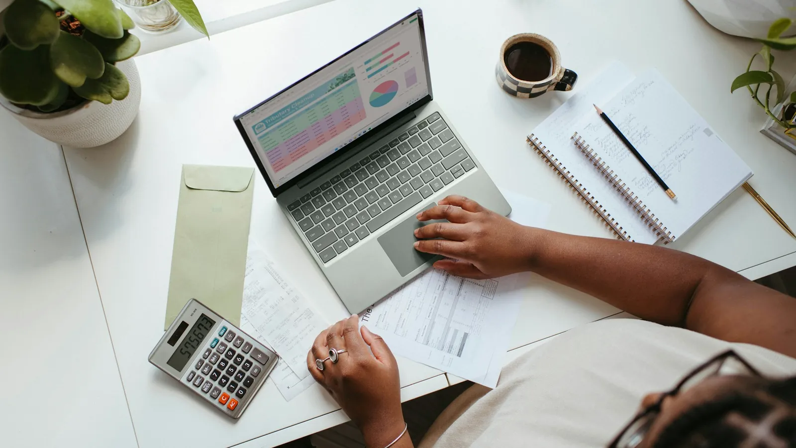A person at a laptop with charts beside a calculator and notes