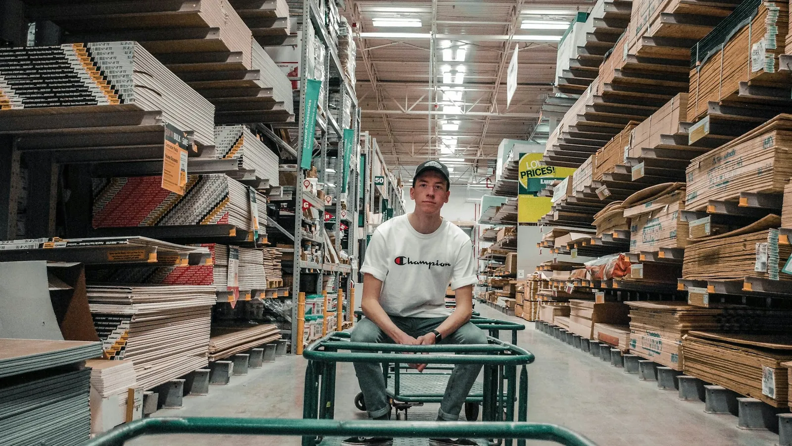 A worker with a cart between tall warehouse shelves
