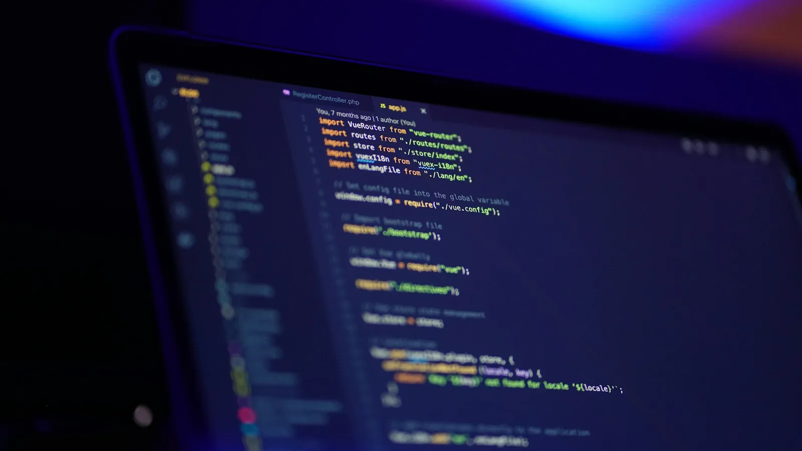 A laptop showing code in a dark room lit in blue and purple