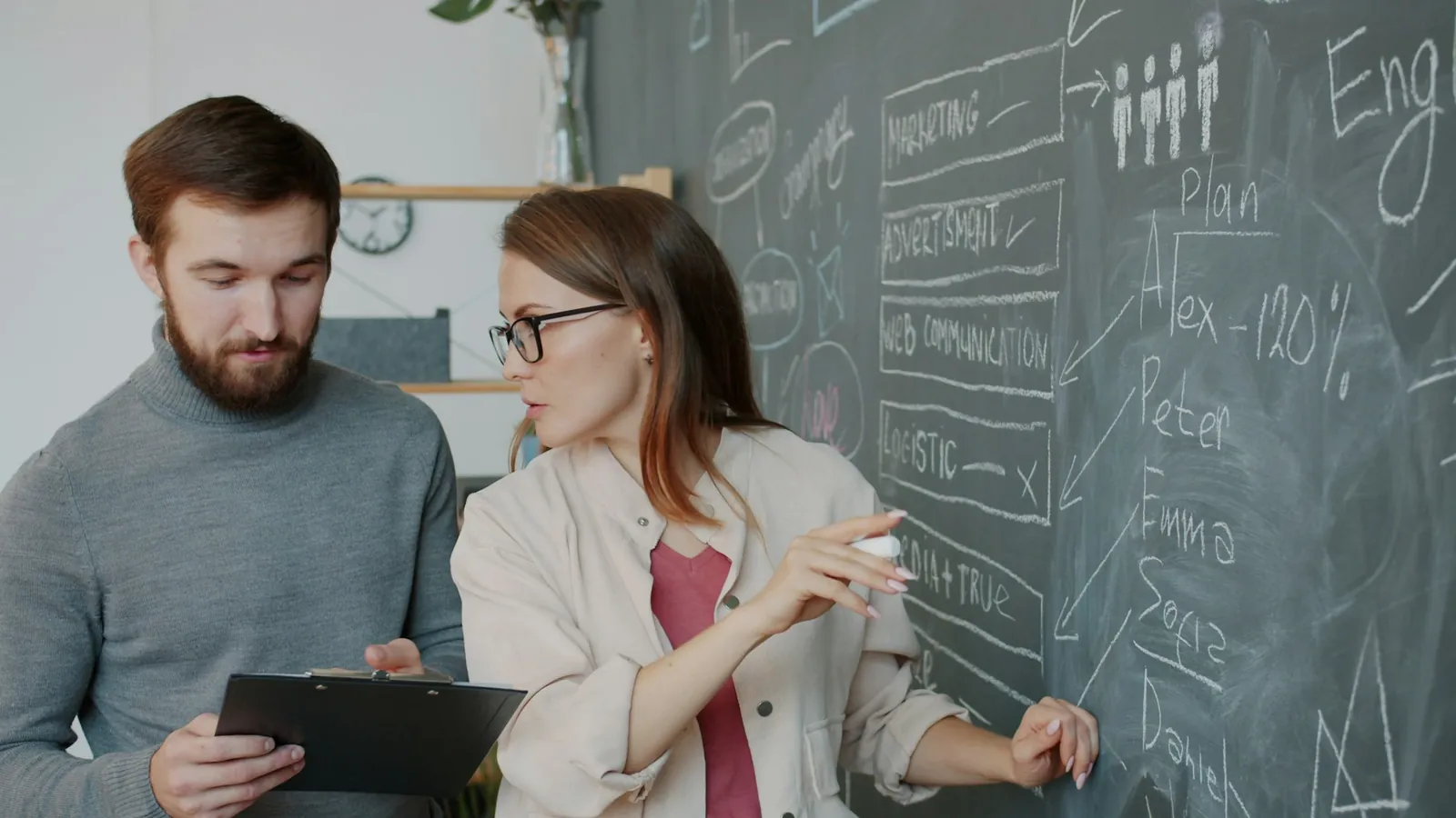 Two colleagues discussing a plan at a chalkboard