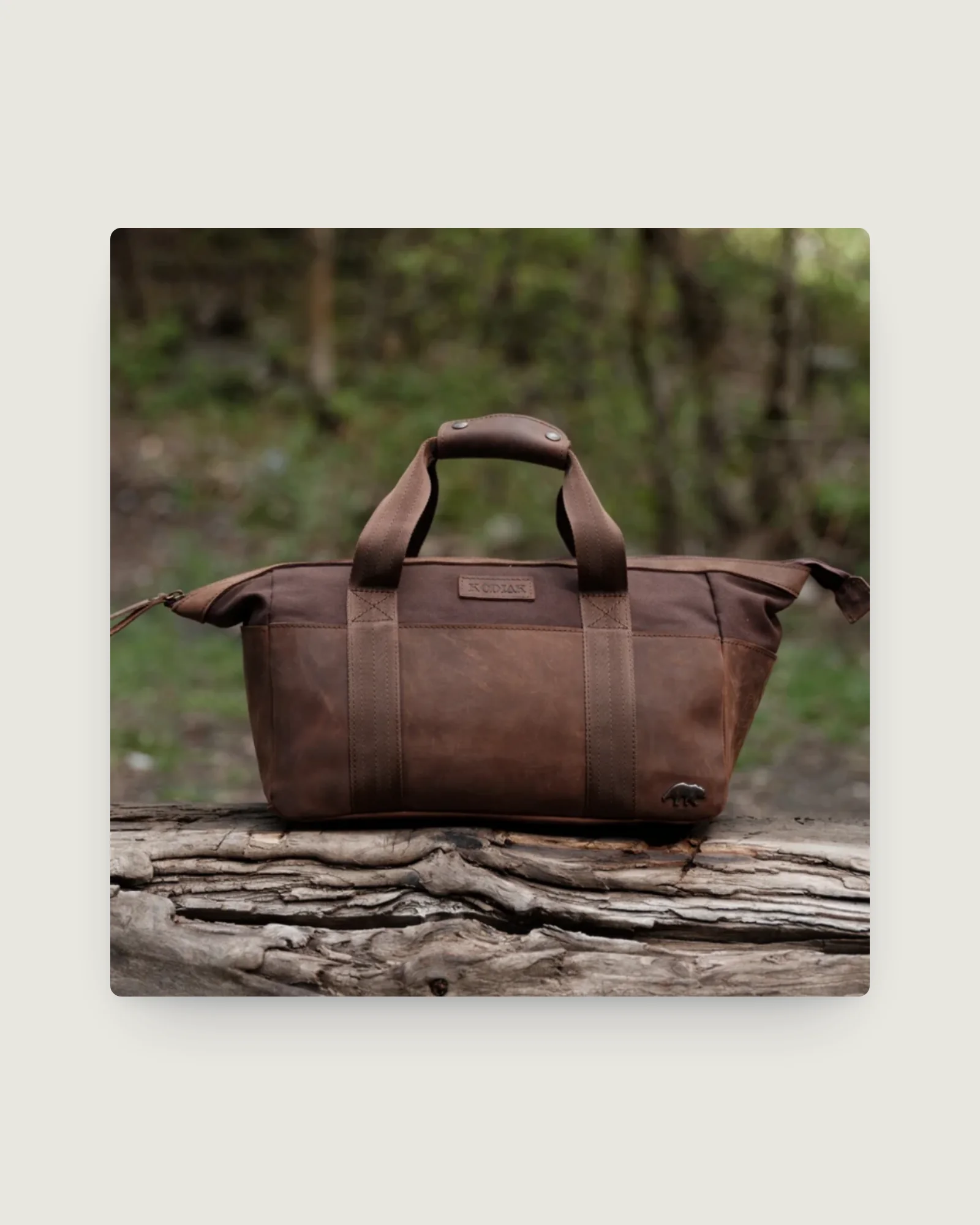 Brown full-grain leather duffel bag on a log outdoors