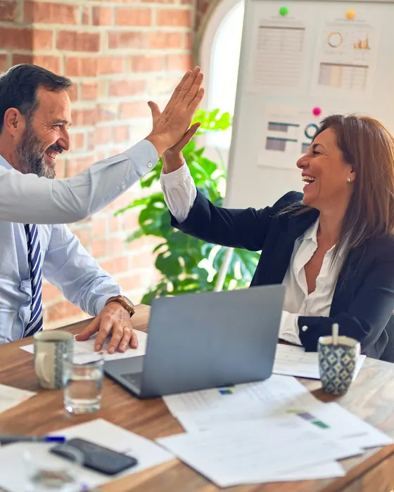 Two business owners celebrating at a desk with a laptop